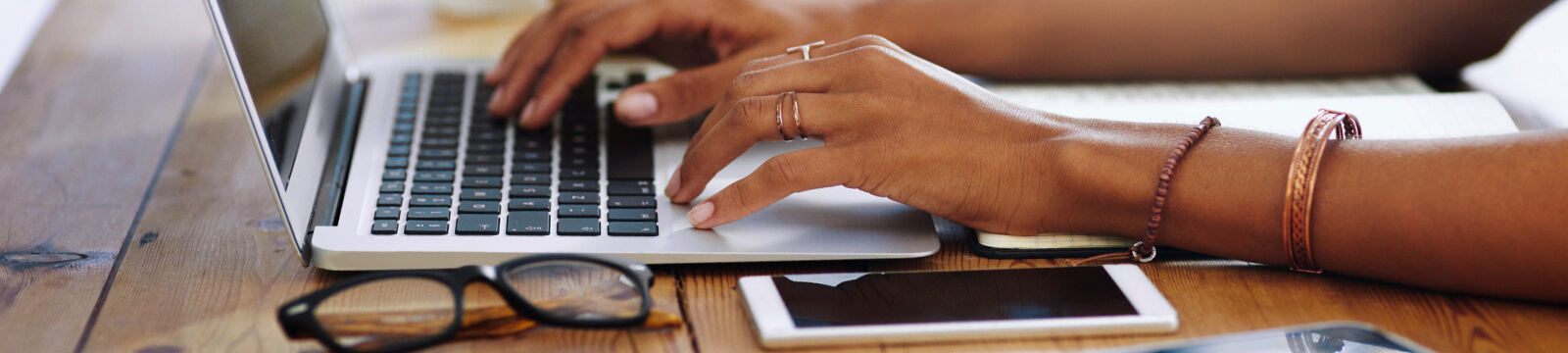 Woman typing on laptop at desk near glasses and phone