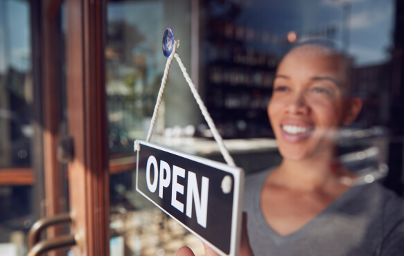 A happy business owner flipping door sign to "open"